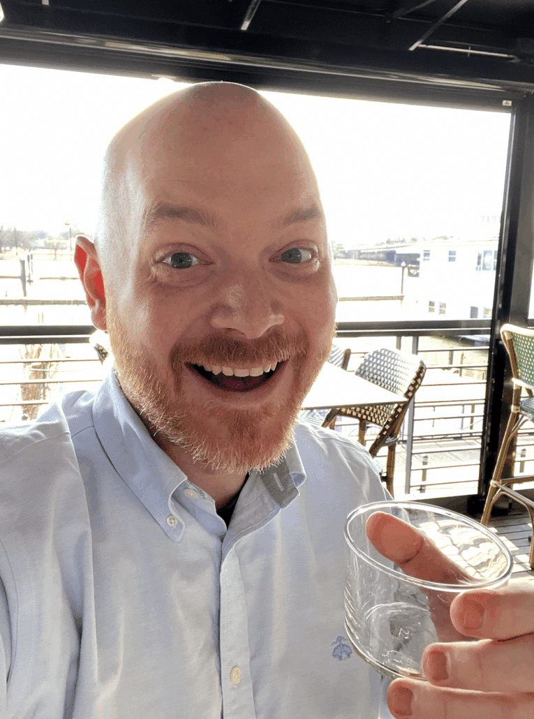 Richard holding a drink on a veranda.